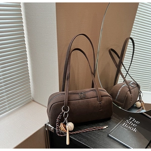 Detail der kaffeebraunen Boston-Tasche aus Wildleder mit Sportanhängern auf Reflexionsfläche
