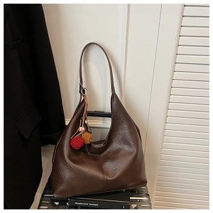 Detail of a large dark brown faux leather tote bag with colorful pompom charm decor