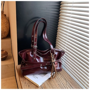 Détail du sac bandoulière en cuir verni bordeaux avec œillets argentés et pompon