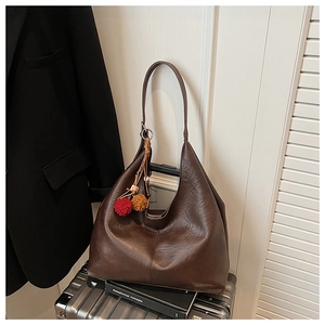 Detail of dark brown leather hobo bag featuring pom-pom charms on a silver suitcase