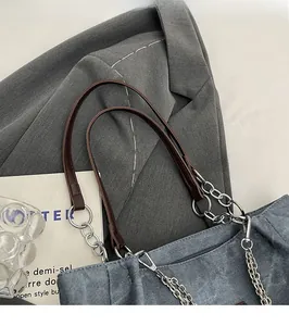 Detail der blauen Denim-Tasche mit braunem Lederriemen und silberner Metallgliederkette