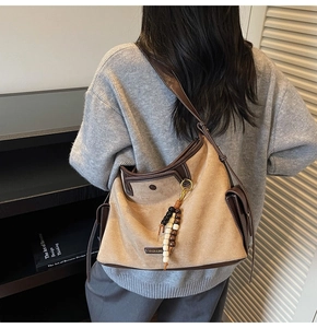 Detail of suede tote bag featuring metallic fashion logo and decorative wooden beads