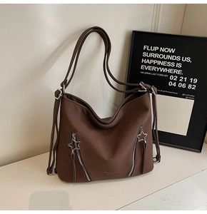 Close-up of brown matte leather tote bag featuring star-shaped silver zippers and sleek logo