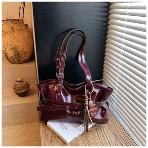 Détail macro du sac bandoulière en cuir brillant bordeaux avec boucle et grigri léopard
