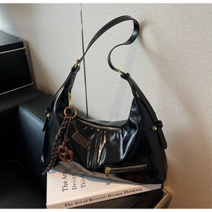 Détail du sac hobo noir brillant avec fermeture éclair et breloque décorative à nœud brun