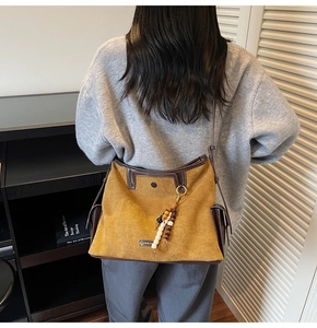 Close-up of a large tan suede tote bag with leather trim and decorative wooden beads