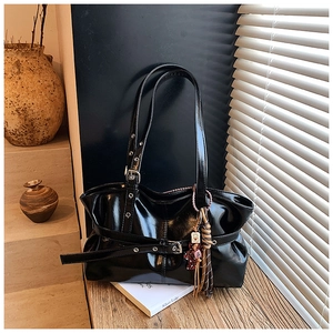 Détail d'un sac bandoulière en cuir verni noir brillant avec boucles et glands déco