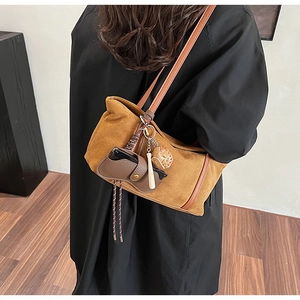 Detail of suede mustard tote bag with leather straps and decorative charms on a shoulder