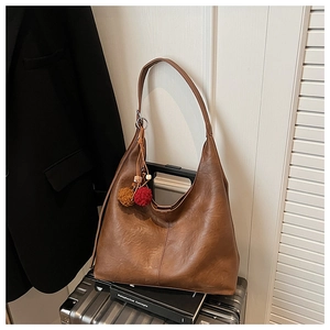 Caramel brown leather Hobo bag with colorful pom-pom charm on a silver suitcase