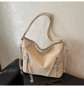Close-up of beige faux leather hobo bag featuring decorative zippers and star metal charms