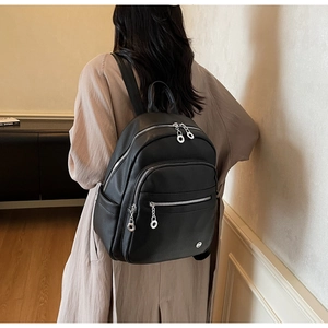 Close-up of black pebble leather backpack featuring multiple silver zippers and ring pulls