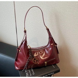 Détail du sac hobo en cuir verni bordeaux avec pampille décorative posé sur un livre de design
