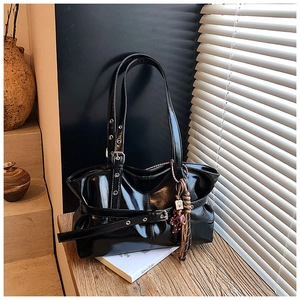 Détail du sac en cuir verni noir brillant avec oillets argentés et boucle sur table en bois