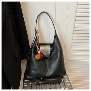 Detail of black leather tote bag with colorful woven charms on a silver suitcase
