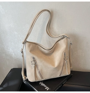 Beige suede hobo bag with star zipper details and wide strap shown in studio setting