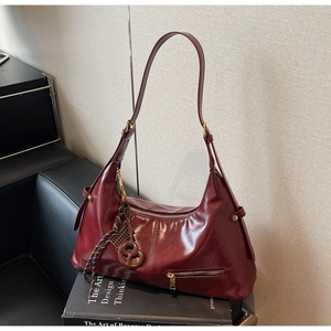 Détail du sac demi-lune bordeaux avec finition brillante et pendentif de style vintage
