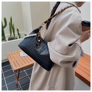 Detail of black woven shoulder bag with chain strap and decorative beads on a beige coat