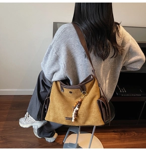 Detail of a mustard suede tote bag with brown leather straps and wooden bead charm accessory