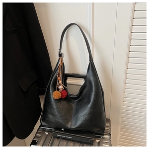 Macro detail of soft black PU leather tote bag with colorful plush ball charm on a suitcase