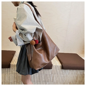 Detail view of a large brown shoulder bag with plush charms and a wide strap on a model