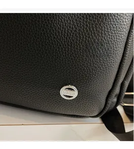 Detail of premium black lychee-textured leather backpack with a silver metal logo buckle