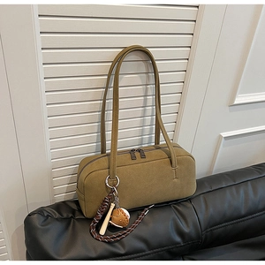 Olivgrüne Wildleder-Schultertasche mit Baseball-Anhänger auf Ledersofa