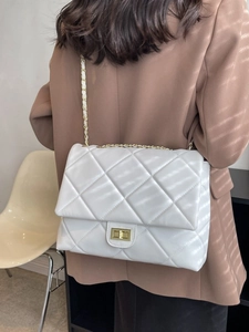 White quilted crossbody bag with gold chain strap and turn-lock closure on female model