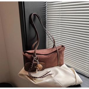 Vue détaillée du sac sous le bras en daim marron avec breloques et texte en relief