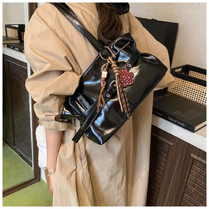 Détail d'un sac à bandoulière en cuir noir brillant avec design plissé et breloque de cœur