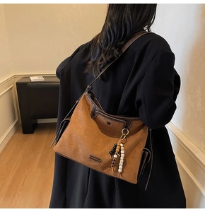 Detail of caramel suede tote bag with leather piping and decorative beaded charm