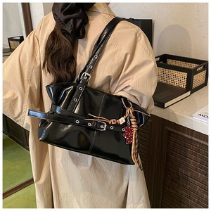 Détail du sac à bandoulière noir brillant avec œillets métalliques et pendentif cœur