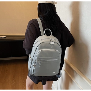 Rear view of a light gray lychee grain leather backpack worn by a model in a modern room