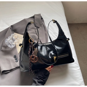 Vue détaillée du sac hobo en cuir verni noir avec fermeture dorée et breloque marron tressée