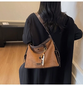 Detail of brown suede shoulder bag with leather trim and vintage wooden bead tassel accessory