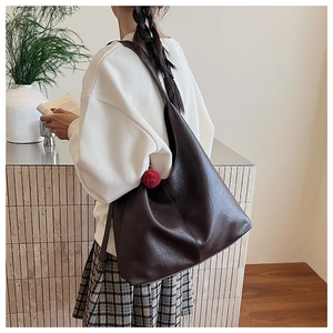 Deep brown oversized tote bag in oily faux leather worn by a model in a minimal setting