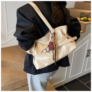 Détail du grand sac beige brillant avec sangles à œillets et charmant pendentif ours