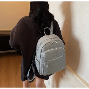 Rear view of a light grey textured leather backpack shown on a model for size and fit