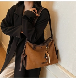 Detail of caramel suede tote with leather trim, wooden bead tassel and metal logo plate