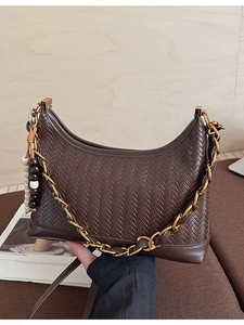 Dark brown suede hobo bag with gold chain and wooden bead charm on a wooden background