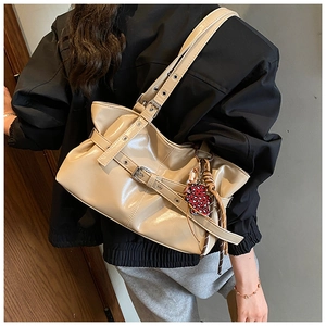 Détail d'un sac porté épaule beige brillant à plis avec boucles et breloque fraise