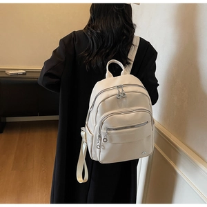 Detail of off-white backpack with lychee grain texture and silver zipper compartments