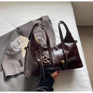 Détail du sac en cuir verni marron foncé avec finitions dorées sur blazer gris