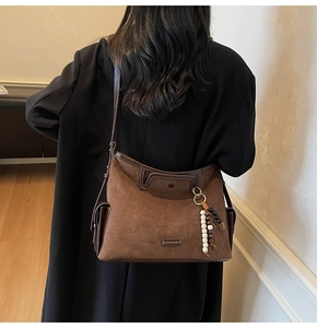 Detail of dark brown suede crossbody bag with vintage beaded charm and metal logo plaque