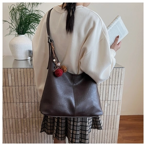 Detail of dark brown tote bag showing faux leather texture and plush ball charm