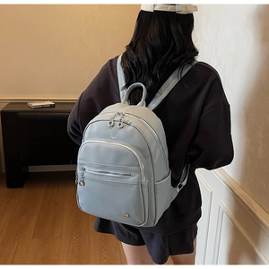 Detailed back view of a dusty blue pebbled leather backpack with functional zip pockets