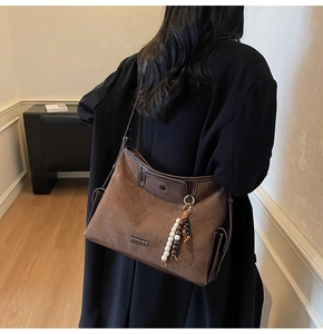 Detail of brown suede tote bag with beaded tassel charm and metallic logo tag