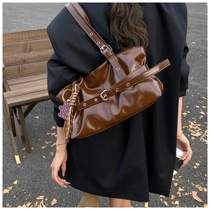 Détail d'un sac porté épaule vintage en cuir verni marron avec bandoulières à œillets argentés