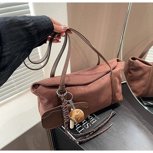 Détail du sac à bandoulière en daim rouge-brun avec breloque baseball et rabat latéral