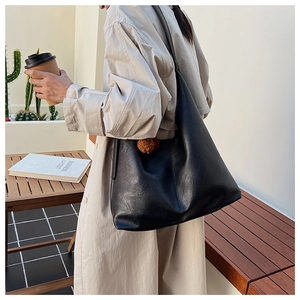 Detail view of large black glossy leather tote bag with brown fur ball charm decoration