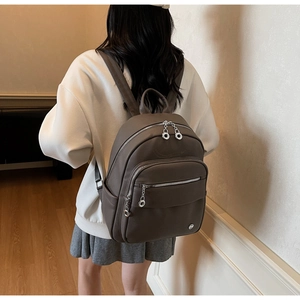 Detail of taupe pebbled leather backpack showing multi-layer zippers and side pockets